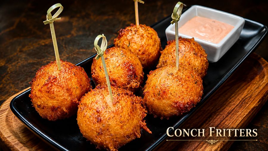 Six conch fritters on skewers with a pink dipping sauce